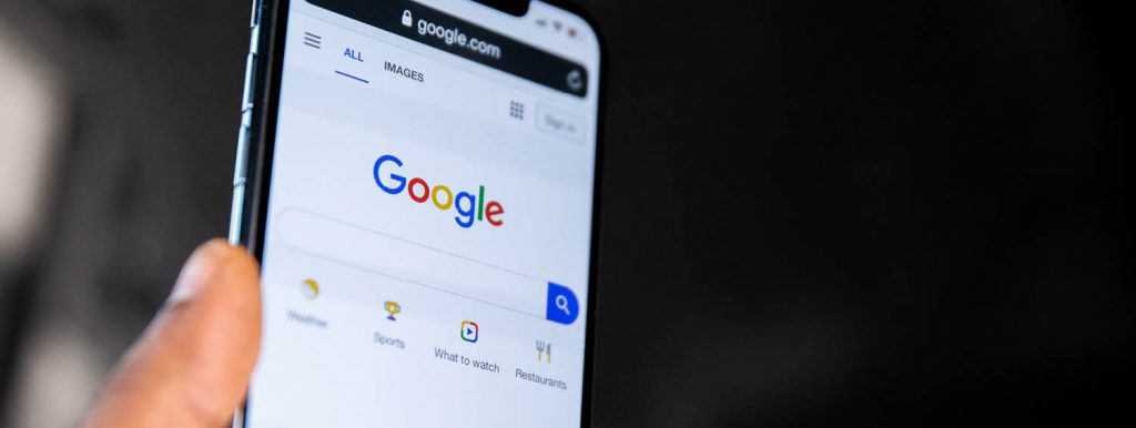 Mão segurando celular com a tela inicial do Google aberta